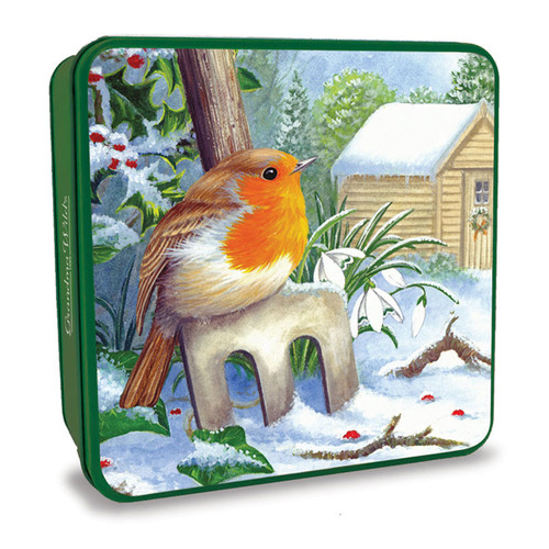 Green square biscuit tin featuring a robin perched on a snow-covered garden stool, with snowdrops, holly and a snowy cottage in the background, ideal for Christmas biscuit or shortbread gifts.