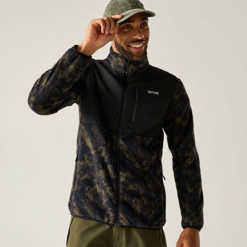 Man wearing a Regatta black and olive camouflage fleece jacket, smiling whilst adjusting a green cap.