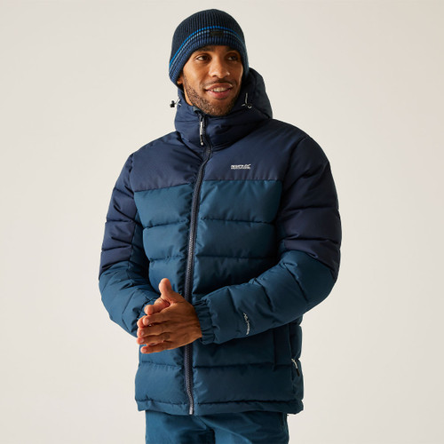 Man wearing a Regatta navy and blue padded hooded jacket with a knitted beanie, standing with hands together.