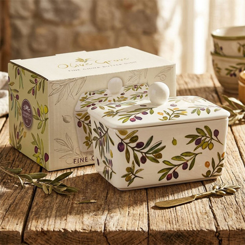 Olive Grove fine china butter dish with a fitted lid and round knob handle, decorated with a colourful olive branch pattern in green, purple and yellow. Displayed on a rustic wooden table with its matching gift box and olive sprigs, creating a Mediterranean-inspired kitchen setting.