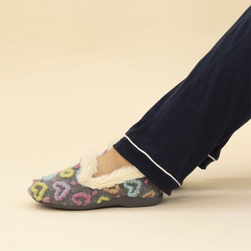 Close-up of women's grey slipper with colourful heart print, soft faux fur trim and cushioned sole, worn with navy pyjamas.