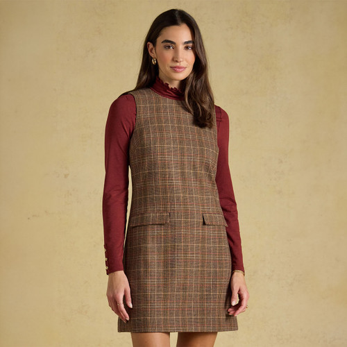 Brown checked sleeveless mini dress styled over a burgundy high-neck top, with a round neckline and front flap pockets.