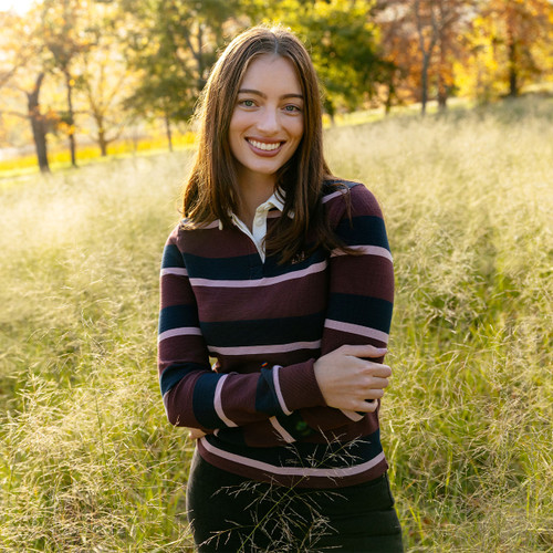Woman wearing a LeMieux burgundy, navy and pale pink striped long-sleeve rugby shirt in an autumn meadow.