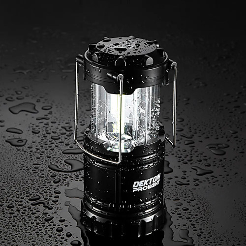 A black DEKTON XA300 Adventurer Lantern with a clear body, sits on a wet surface, showcasing its waterproof design.