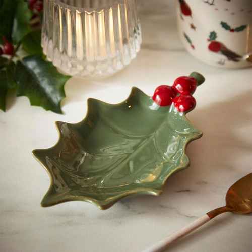A ceramic tea bag tidy shaped like a green holly leaf with red berry accents, arranged on a marble surface.