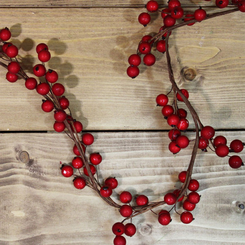 Red berry garland with glossy faux berries on flexible brown stems, arranged on a rustic wooden surface for festive Christmas decorating.