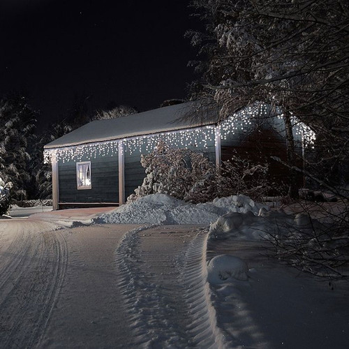 The NOMA 480 Snowing Icicle LED Lights White - 10.2m decorated on a house surrounded by snow