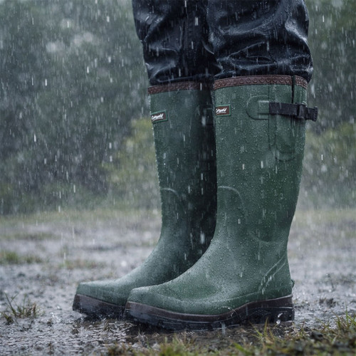 Close-up of green rain boots standing in a puddle during a heavy rainstorm. The scene conveys a sense of wet outdoors and stormy weather.
