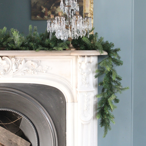 Artificial pine Christmas garland draped over an ornate fireplace mantel, creating a classic festive display with lush green foliage and seasonal décor.