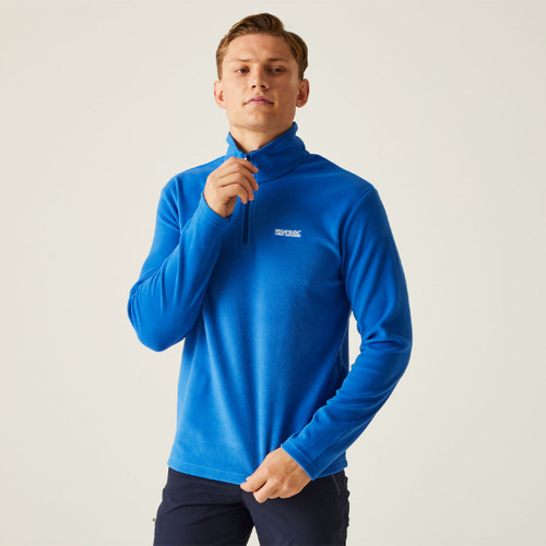 A person in a bright blue zip-up fleece stands confidently against a plain background. The casual attire suggests a sporty or outdoors context.