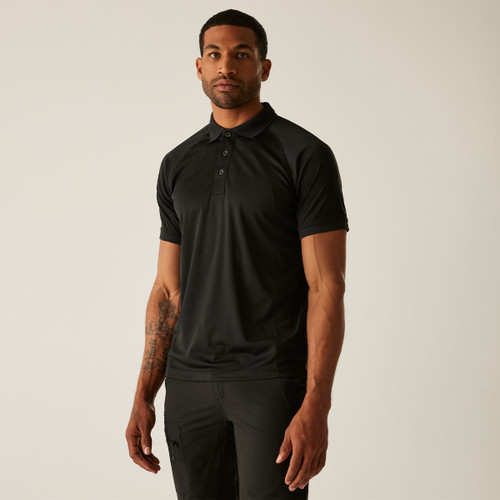 Man in a black polo shirt with short sleeves stands against a plain background. His right arm displays a visible tattoo. The mood appears confident.