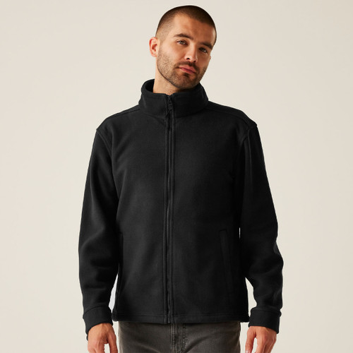 Front view of a man wearing a black full-zip fleece jacket with high collar, long sleeves, and minimalist design, styled with grey jeans for casual everyday wear