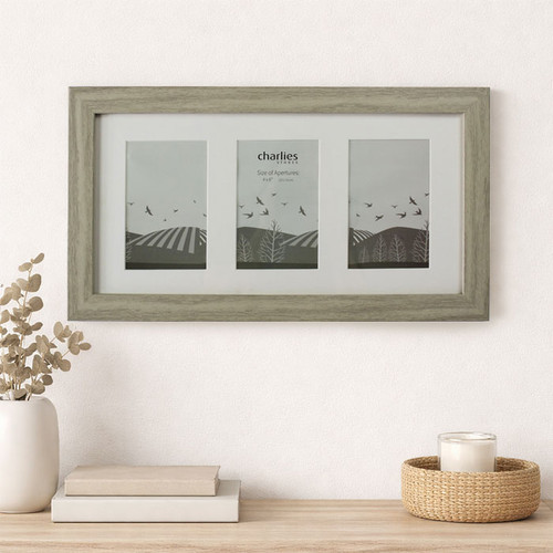 Light wood triple aperture picture frame with white mount displaying three minimalist landscape prints, styled on a wooden surface with books, a vase of dried foliage, and a candle against a neutral wall.