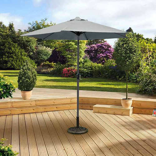 A grey patio umbrella stands on a wooden deck surrounded by potted shrubs. The lush garden in the background creates a serene, inviting atmosphere.