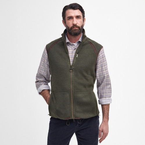 Man with a beard wearing a green zip-up gilet over a plaid shirt. The outfit conveys a rugged, outdoorsy style. White background.