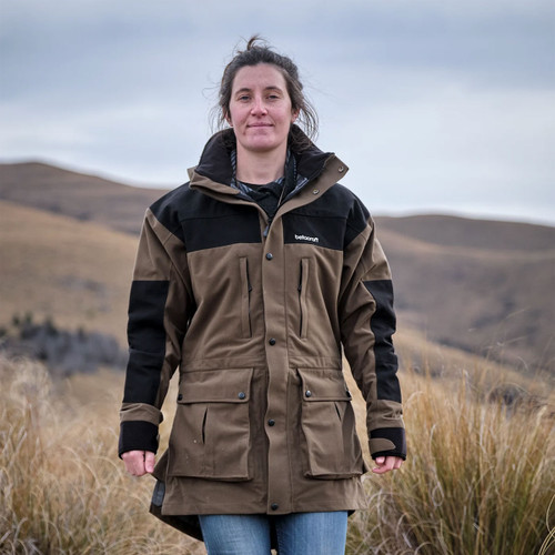 A person in a brown and black outdoor jacket stands in a grassy, mountainous landscape under a cloudy sky, conveying a sense of calm and resilience.