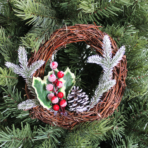 A small festive wreath with holly, red berries, and pinecones set against green pine branches.