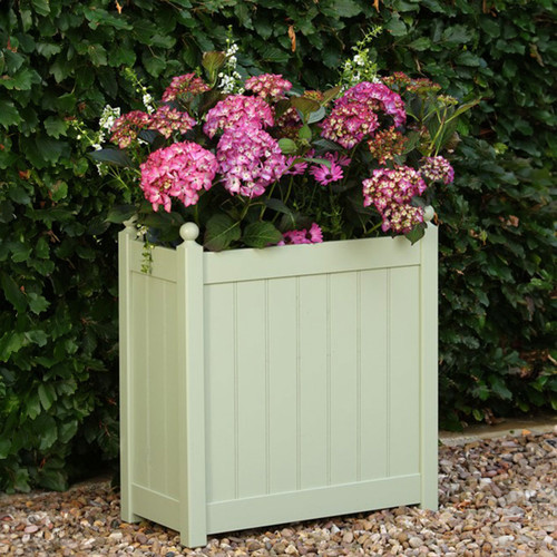 Sage green square garden planter filled with pink hydrangeas, set on gravel in front of a leafy hedge.