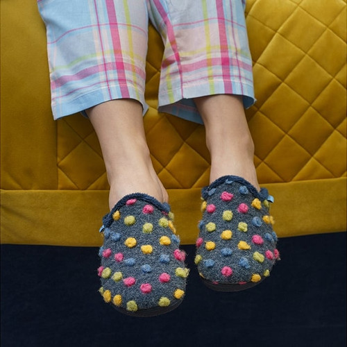 An image of a pair of slip on, Lunar mule slippers with a multicoloured polka dots. They are paired with light blue, tartan pyjamas.