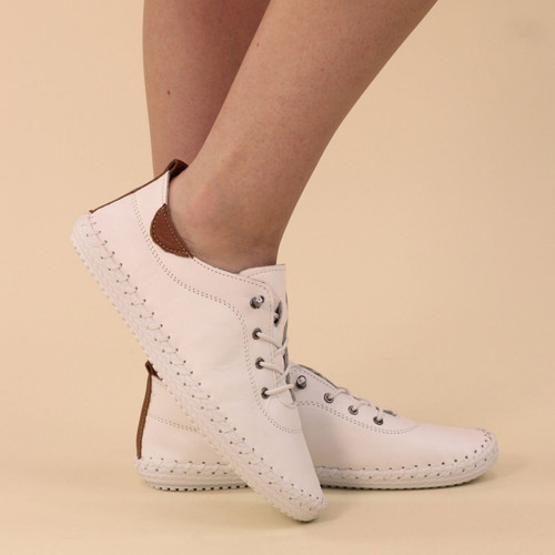 White leather lace-up trainer shoes with tan heel tab and stitched white sole, worn on model against beige background.