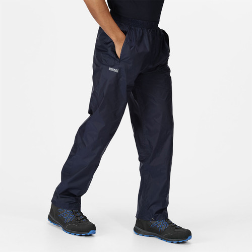 A person wearing dark blue waterproof trousers and black hiking shoes walks with hands in pockets against a plain white background.