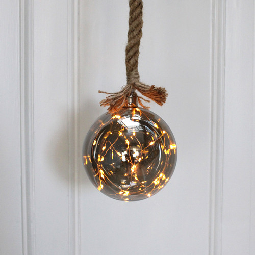 A glass ball LED rope light with warm white lights, hung against a white wooden background.
