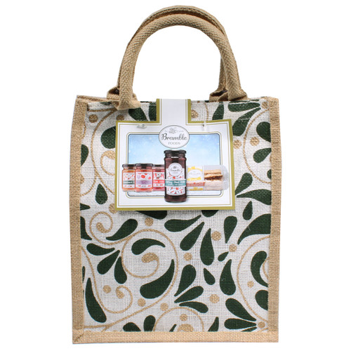 A decorative jute bag with leafy green and beige patterns, featuring a label displaying jars of jam and a dessert. The tone is rustic and inviting.
