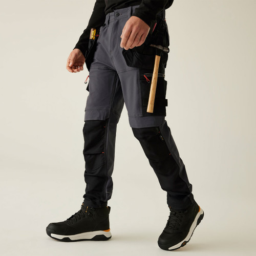 Men’s grey and black work trousers with reinforced knee panels, multi-pocket utility design, and hammer loop, shown in action with tools attached and durable stretch fabric for trade work.