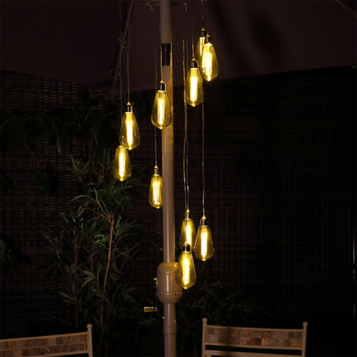 Tall cluster chandelier light with glowing amber bulbs, hanging above wooden chairs in a dimly lit room.