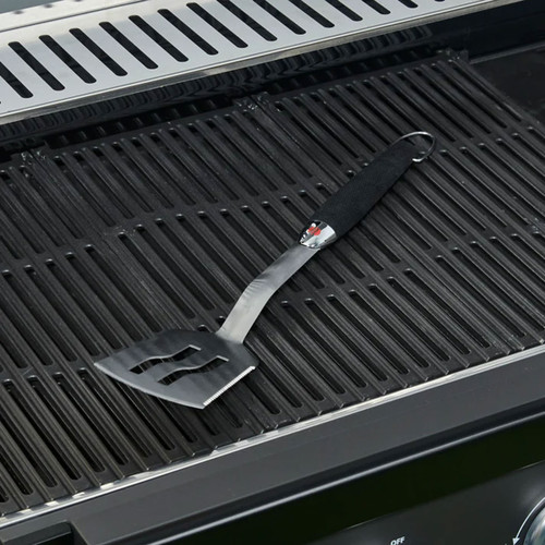 Metal barbecue spatula with a black handle resting on cast iron grill grates.