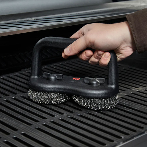 Hand using a dual-head scour brush with two metal scrub pads to clean cast iron barbecue grill grates.