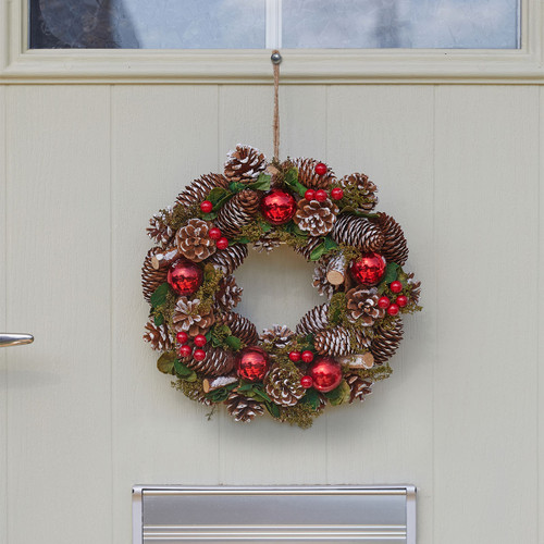 A festive Christmas wreath with pinecones and red ornaments hangs on a light-coloured door.