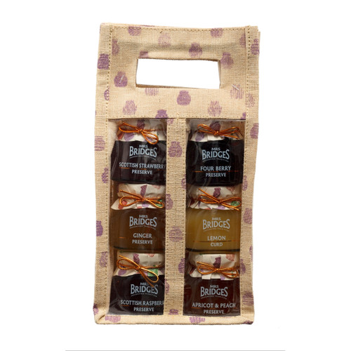 A natural jute-style Mrs Bridges gift bag with purple jar motifs, holding six assorted miniature jars of preserves and chutneys arranged in two vertical rows behind a clear front panel.