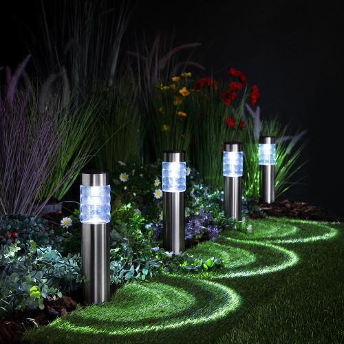 Four stainless steel pathway lights with clear tops, casting a glow along a garden lawn at night.