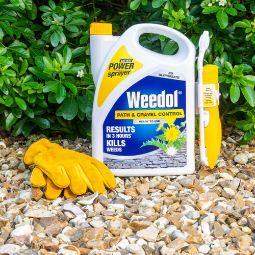 A container of Weedol Path & Gravel Control with a yellow sprayer sits on gravel, alongside a pair of yellow gloves. Green foliage forms the background.