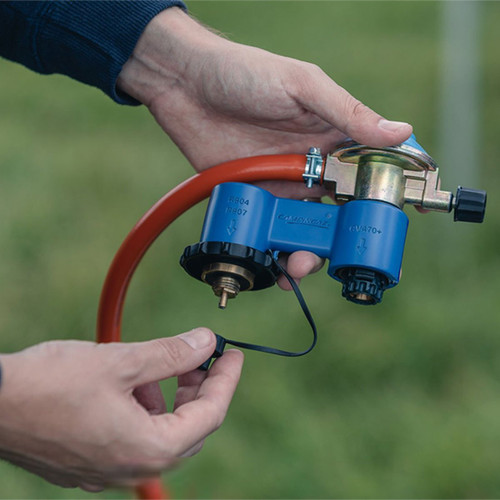 A person holds a blue valve with a red hose, showcasing its components against a blurred green background.
