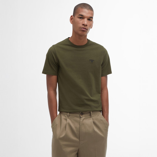 A man in olive green T-shirt and beige trousers stands with hands in pockets against a white background, conveying a relaxed and casual vibe.