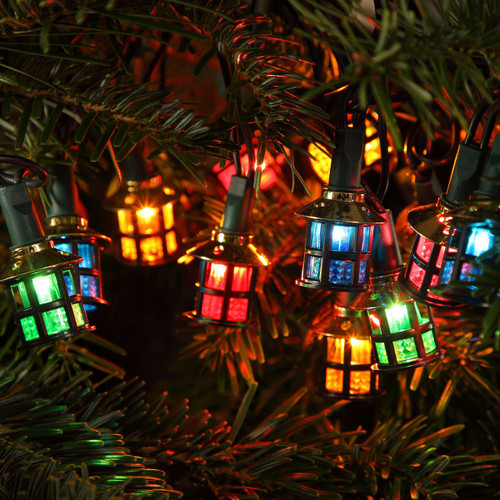 Multicoloured lantern-shaped LED string lights displayed among Christmas tree branches, featuring decorative miniature lantern bulbs that create a warm and festive holiday glow.