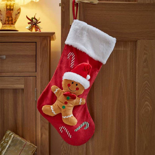 A festive red Christmas stocking with a gingerbread man design and white fur trim, hung on a wooden door with holiday decorations nearby.