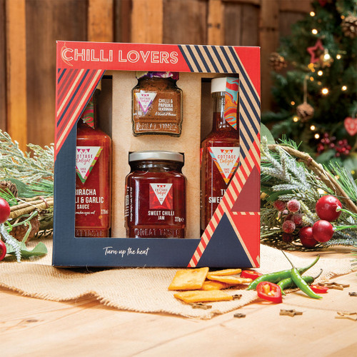 Festive setting with a "Chilli Lovers" gift box containing sauces and seasonings. Pine branches and red berries beside it convey a holiday vibe.