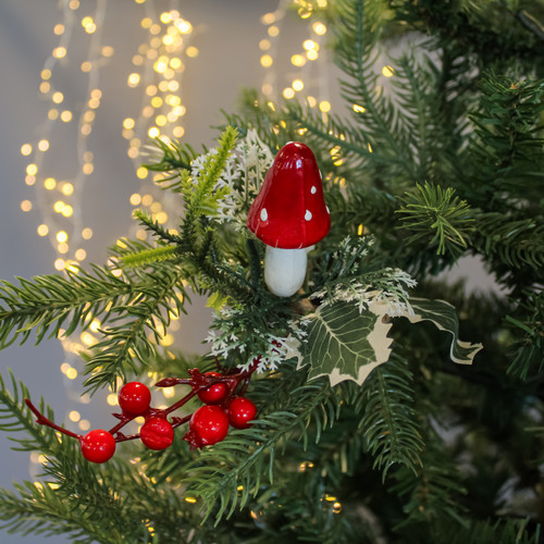 Festive tree branch with a red and white mushroom ornament, red berries, and green leaves, set against soft, warm fairy lights in the background. Festive tree branch with a red and white mushroom ornament, red berries, and green leaves, set against soft, warm fairy lights in the background.