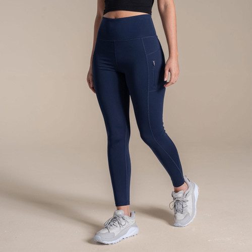 Woman wearing navy high-waisted gym leggings with side zip pocket, studio background.