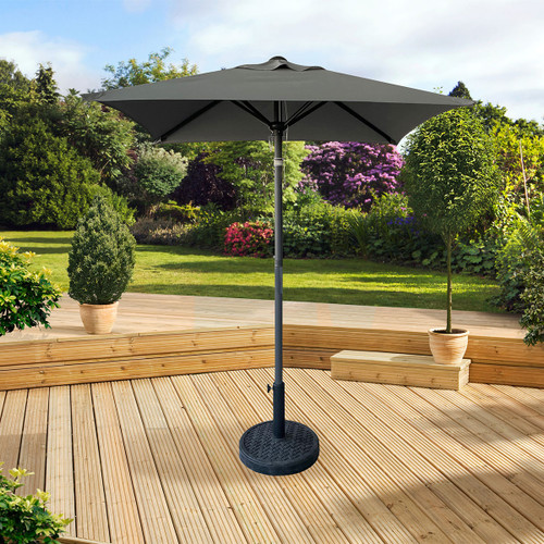 A sunlit wooden deck features a large grey umbrella. Potted plants and lush green trees in the background create a serene, inviting garden scene.