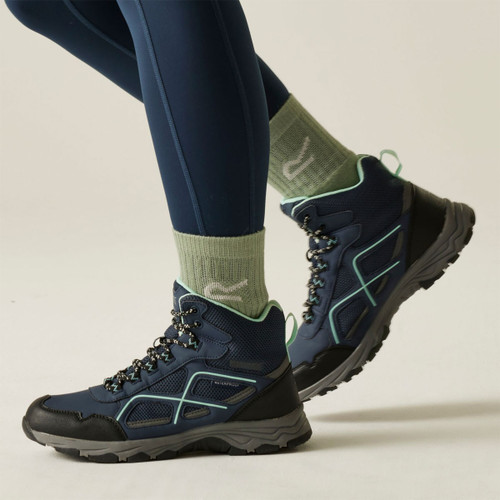 Navy hiking boots with mint green detailing and rugged tread soles, worn with green walking socks and navy leggings.
