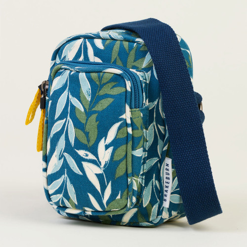 Blue leaf-patterned sling bag with yellow zip pull on a white background.
