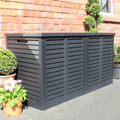 Large black slatted garden storage box placed on a patio beside a brick wall and potted plants.
