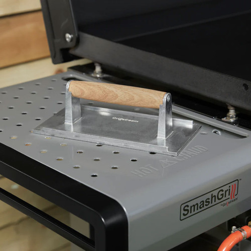 Smash grill burger press resting on a SmashGrill griddle plate.