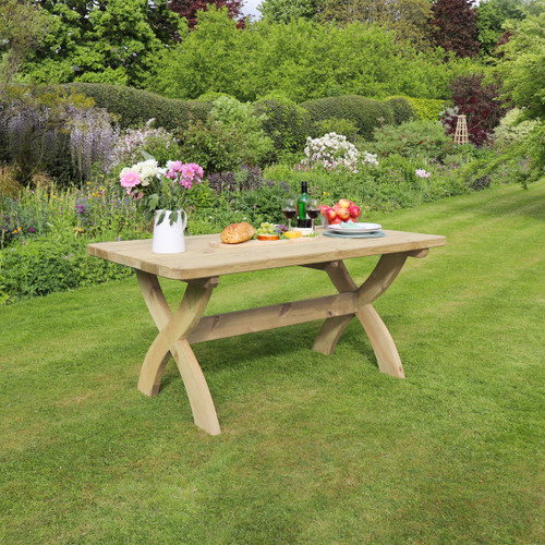Rectangular wooden garden dining table with curved cross-leg supports, positioned on grass and set with food and drinks.