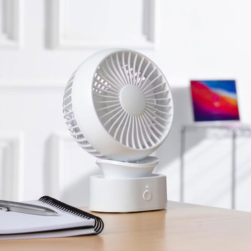 White Daewoo mini desk fan on a wooden desk next to a notebook, shown in a home office setting.