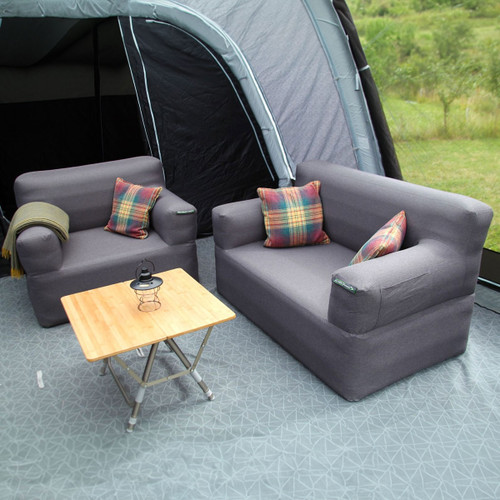 Cosy outdoor seating arrangement with a gray sofa, two armchairs, plaid cushions, and a wooden coffee table inside a tent.
